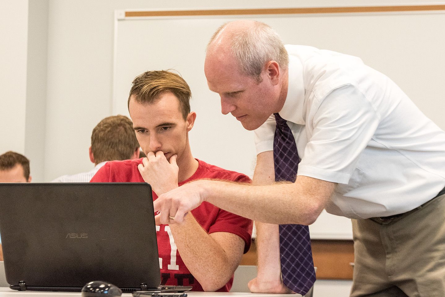 An instructor helps a student at a laptop
